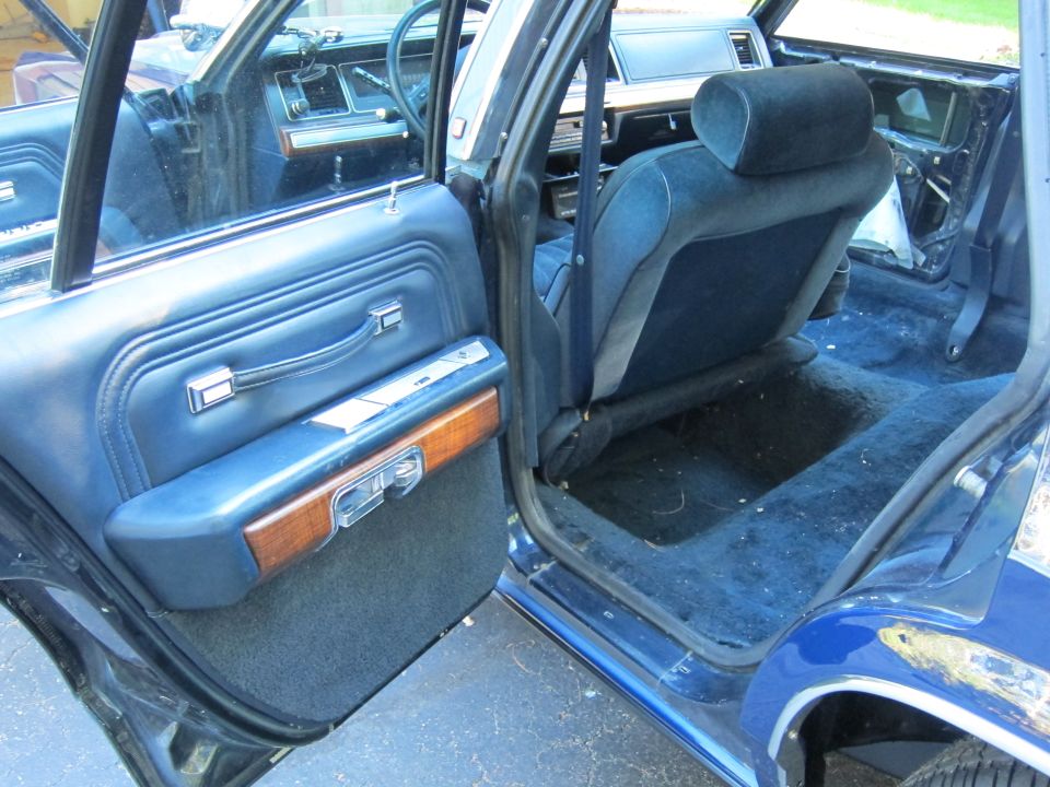 Interior view of a blue sedan, showing the driver's side door open, blue seats, and carpeted floor