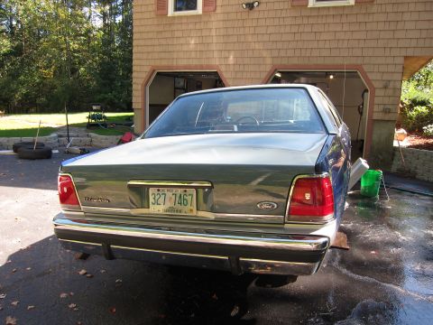 1991 Ford LTD Crown Victoria - The rear of a 1991 Ford Crown Victoria LTD is visible, parked in a driveway with a garage in the background.