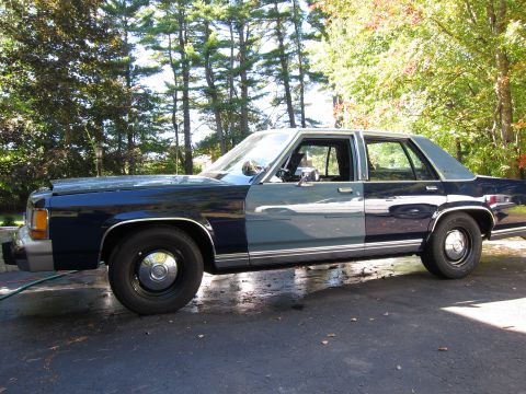 1991 Ford LTD Crown Victoria - A two-tone sedan sits parked on a driveway with trees in the background.