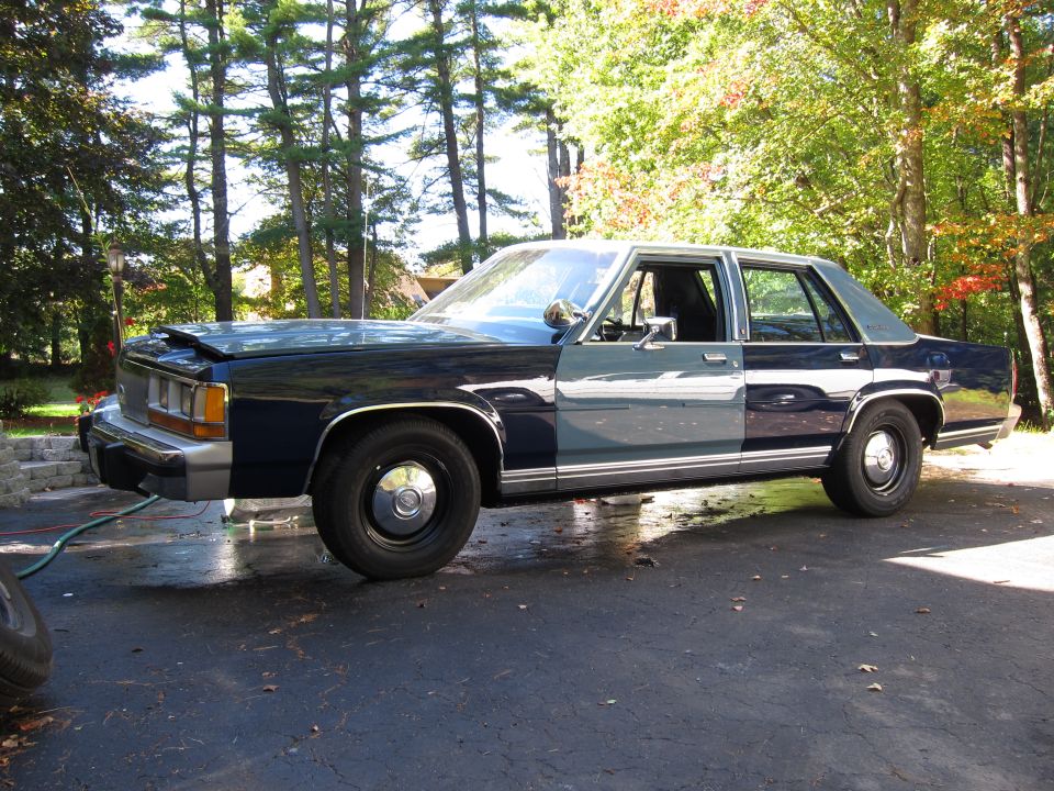 Dark blue and gray sedan with hood ajar, parked on asphalt driveway