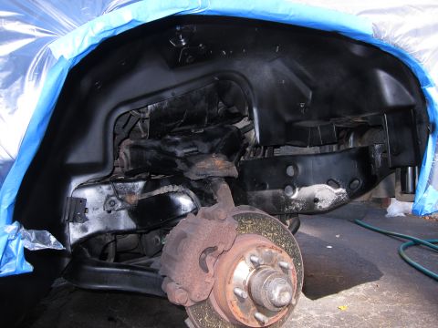 1991 Ford LTD Crown Victoria - The wheel well and suspension of a vehicle are visible, with some parts covered by blue plastic sheeting.