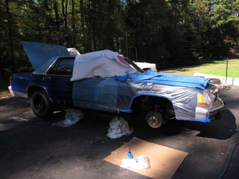 1991 Ford LTD Crown Victoria - A blue sedan is covered in protective materials, with its hood up, indicating it is being prepped for a paint job.