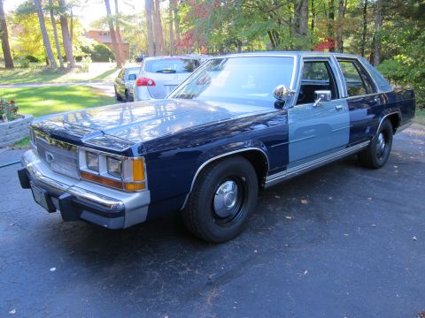 1991 Ford LTD Crown Victoria - A two-tone Ford Crown Victoria is parked in a driveway with trees in the background.