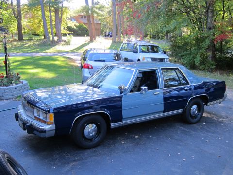 1991 Ford LTD Crown Victoria - This 1991 Ford Crown Victoria LTD, painted in a two-tone blue, is seen from a three-quarter front perspective with other vehicles in the ba…