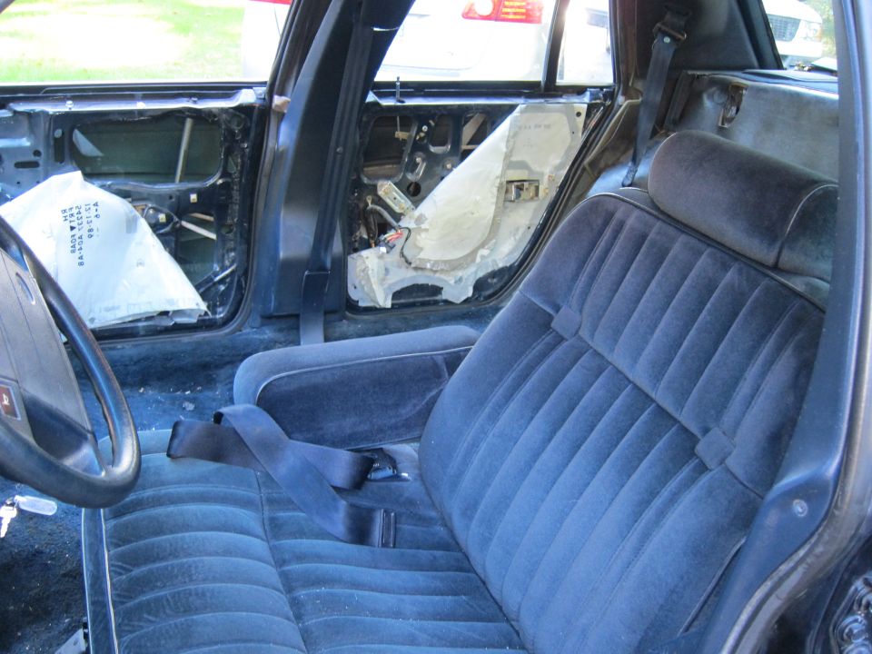 Interior of a car with door panels removed, showing exposed wiring and insulation. Blue velour seats are visible
