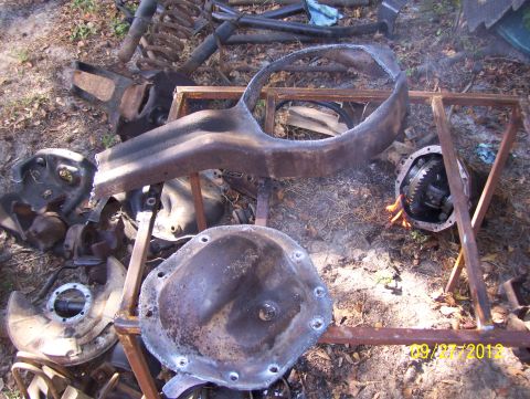 1990 Ford Bronco - Various rusty vehicle parts, including differential covers and suspension components, lie on the ground outdoors.