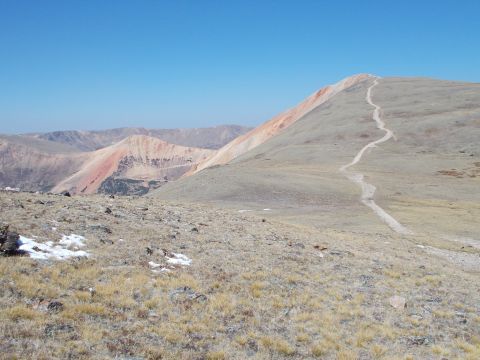 1986 Ford Bronco II - A scenic view of a mountain range with a trail leading to the summit under a bright blue sky.