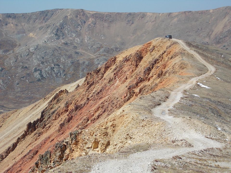 Dark SUV on a dirt road atop a mountain, viewed from behind
