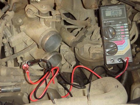 1989 Ford Bronco - A Micronta digital multimeter reading 680 rests against dusty engine components, with its red and black test leads clipped to a connector i…