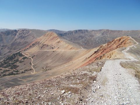 1986 Ford Bronco II - A scenic mountain vista with a winding dirt road and a single vehicle visible in the distance on a ridge.