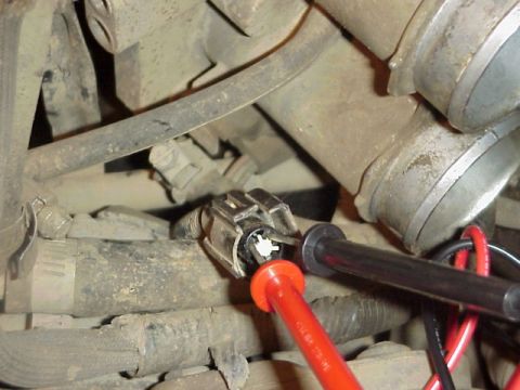 1989 Ford Bronco - Engine-bay close-up of red and black multimeter probes being back-probed into a grey three-wire throttle position sensor connector on a dus…