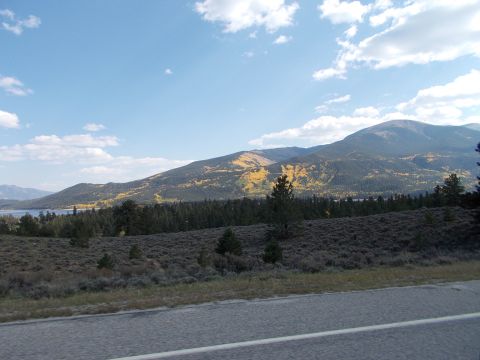 1986 Ford Bronco II - A scenic view of mountains with yellowing trees under a blue sky with clouds, beside a paved road.