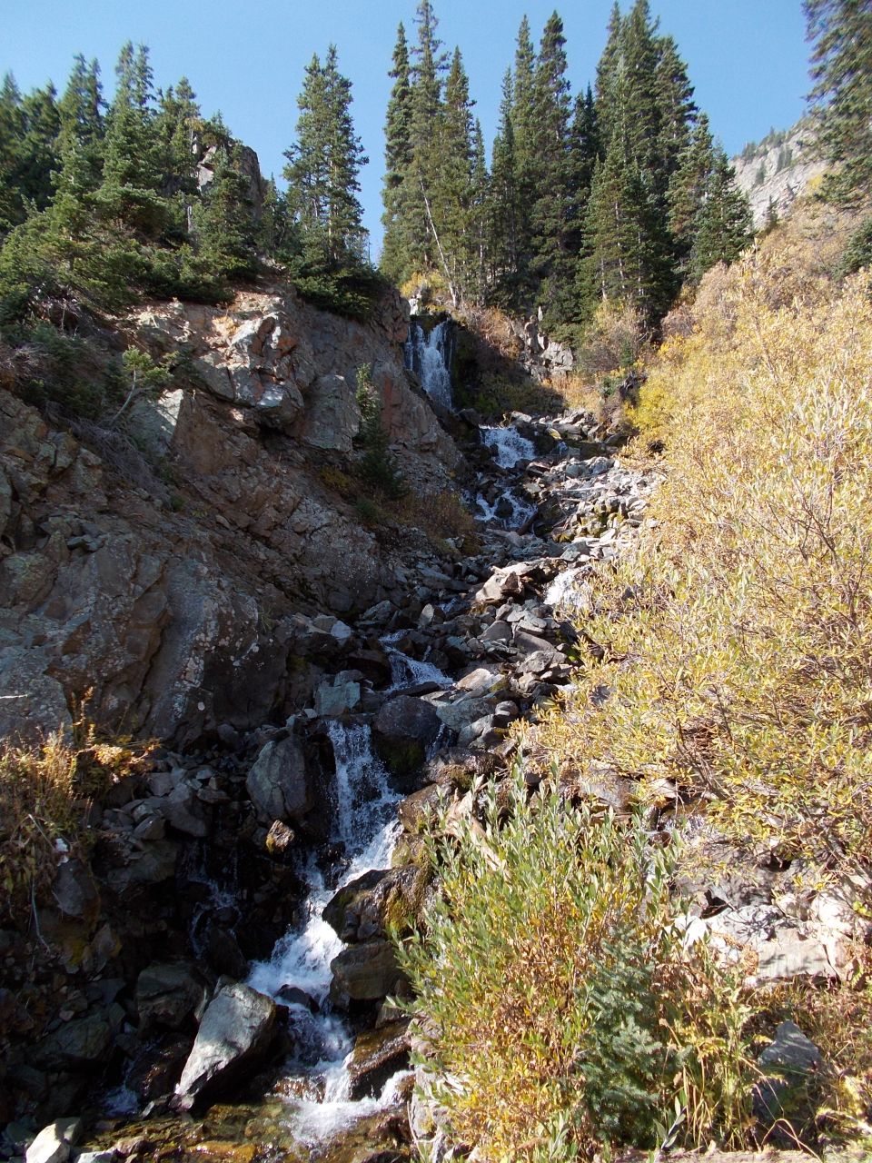 waterfall cascading down a rocky slope with pine trees and autumn foliage