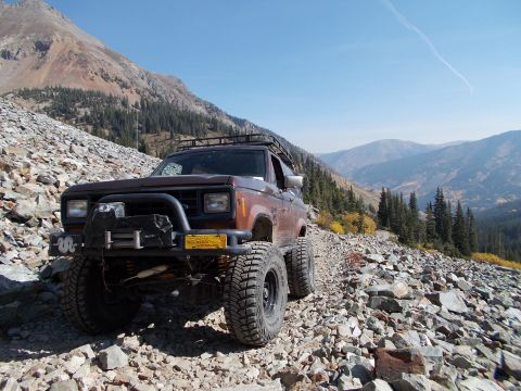 1986 Ford Bronco II - A brown 1986 Ford Bronco II navigates a steep, rocky mountain path under a clear blue sky.