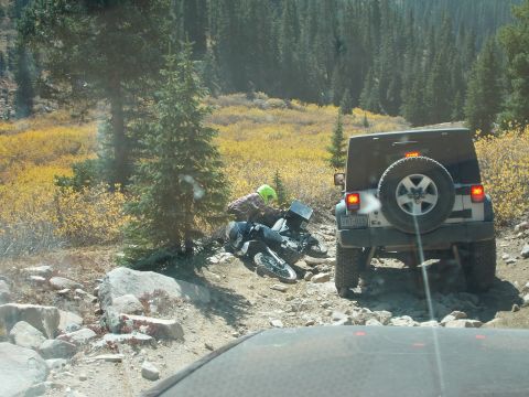 1986 Ford Bronco II - A motorcycle has fallen on a rough mountain trail, with a Jeep stopped nearby.
