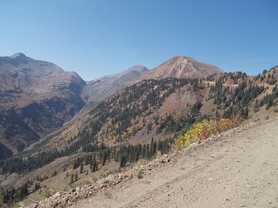 mountain valley with trees and a dirt road in the foreground, clear blue sky above
