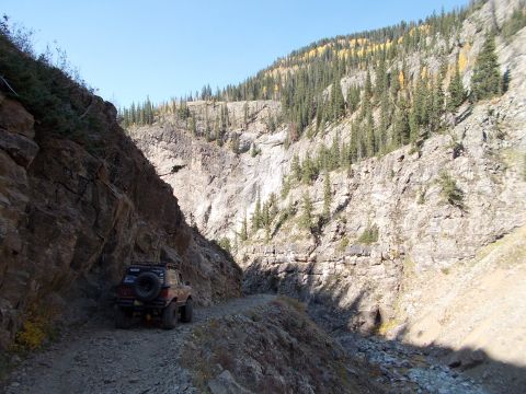 1986 Ford Bronco II - A lone off-road vehicle navigates a steep, rocky mountain pass under a clear blue sky.