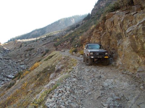 1986 Ford Bronco II - An SUV navigates a narrow, rocky mountain pass with steep inclines and sparse vegetation.