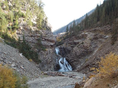 1986 Ford Bronco II - A scenic waterfall flows through a canyon, surrounded by rocky slopes and evergreen trees.