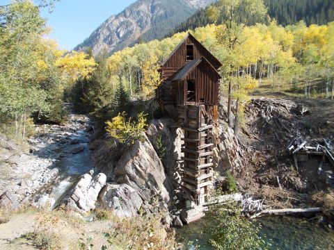 1986 Ford Bronco II - An old wooden structure is perched precariously on a rocky cliff overlooking a stream, surrounded by trees in autumn colors.