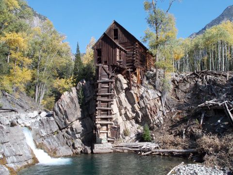 1986 Ford Bronco II - An old wooden mill structure clings precariously to a cliff face, overlooking a body of water with a small waterfall.