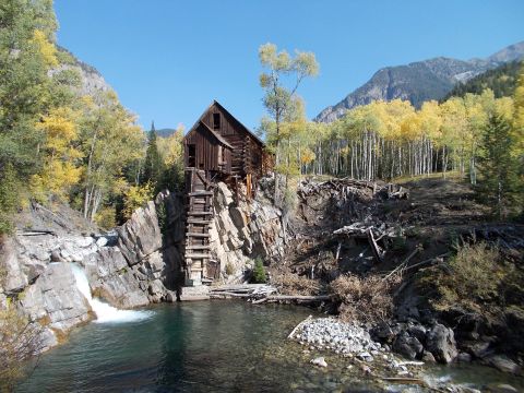 1986 Ford Bronco II - Historic wooden mill structure situated on a cliff overlooking a waterfall and clear water, surrounded by fall foliage.