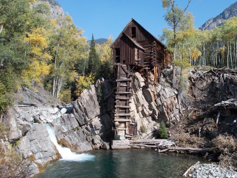 1986 Ford Bronco II - A historic wooden mill sits precariously on a cliff overlooking a waterfall and a body of water, surrounded by autumn foliage.