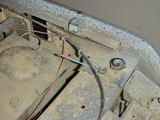 Close-up of engine bay wiring with red and blue wires connected, showing a nut and bolt on metal frame