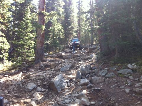 1986 Ford Bronco II - Vehicle driving on a challenging, rocky path through a dense forest.