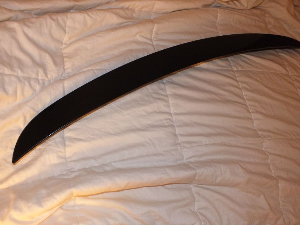 Gloss black curved rear spoiler lip laid on a tan quilted bedspread
