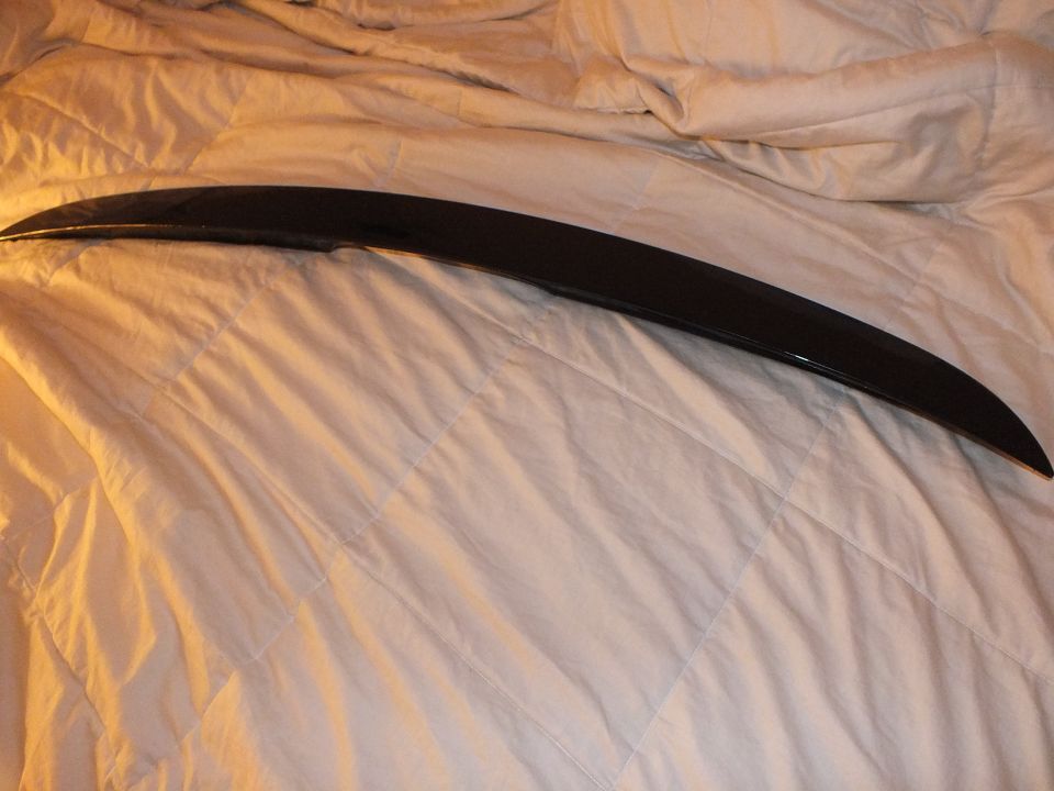 Curved gloss black trunk spoiler resting on light gray quilted bedding