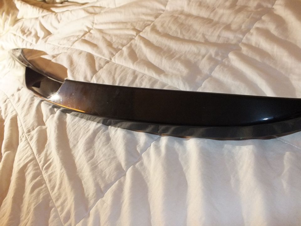 Gloss black spoiler lip angled across rumpled white bedding