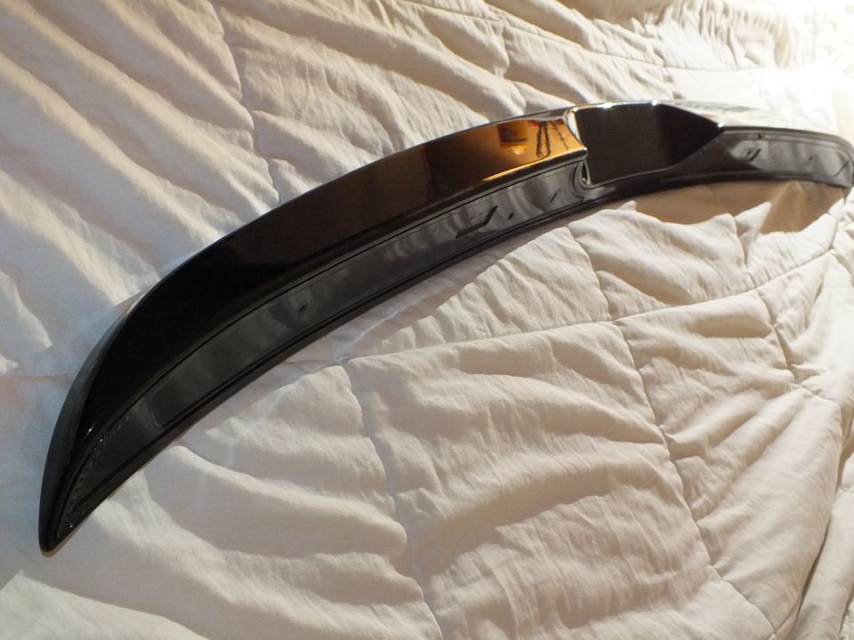 Underside of a curved gloss black spoiler with mounting lip on tan bedding