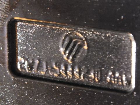 2003 Ford Crown Victoria - Close-up of an embossed Mercury emblem beside ribbed mold marks on a black part
