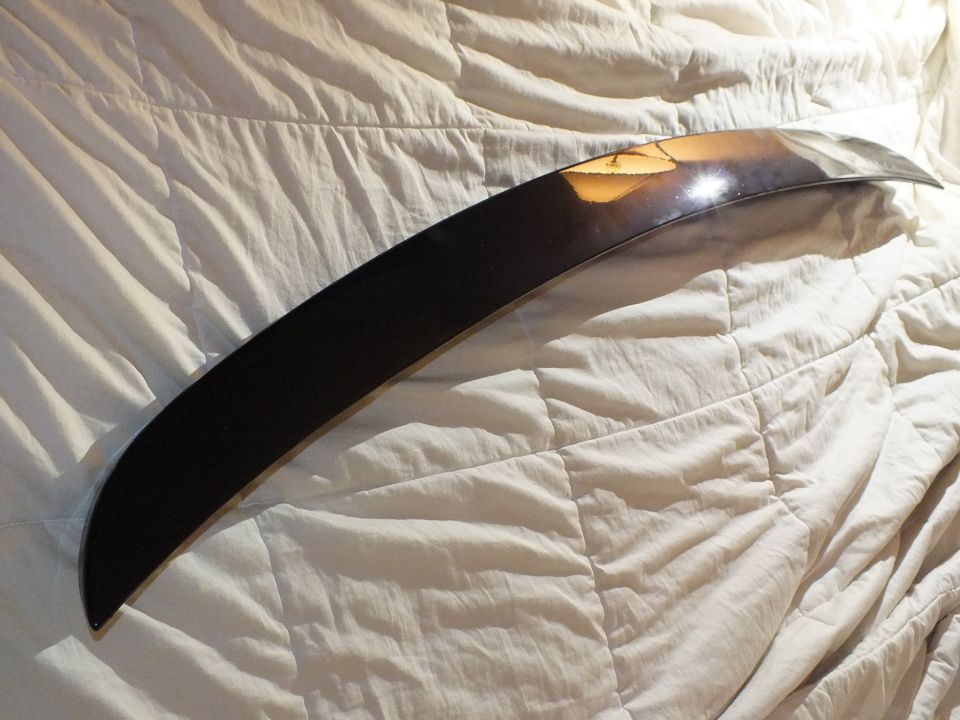 Glossy black curved automotive trim piece reflecting light on white bedding