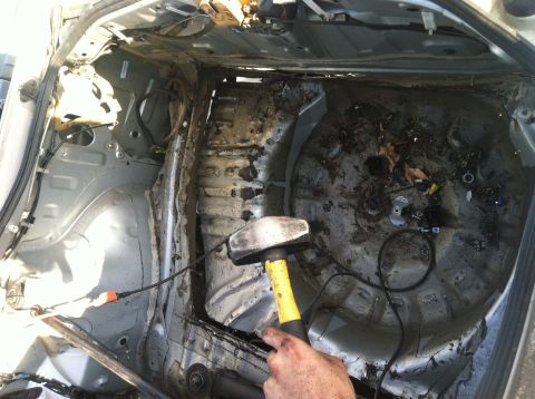 1993 Ford Probe - A hand holds a sledgehammer inside a severely damaged and dirty car trunk interior.