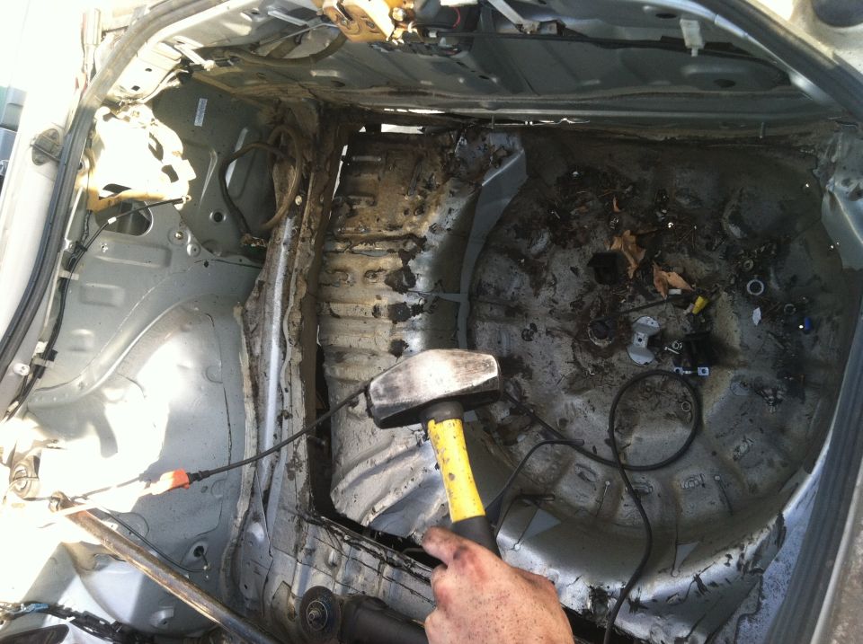 Damaged car trunk interior with rust and debris, a sledgehammer is held by a hand