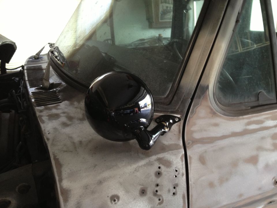Black round bullet mirror mounted on primered truck fender