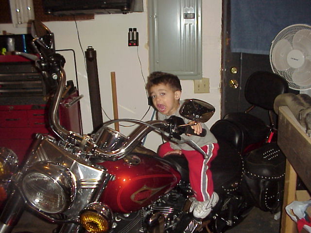 Child sitting on a red motorcycle with chrome handlebars and mirrors