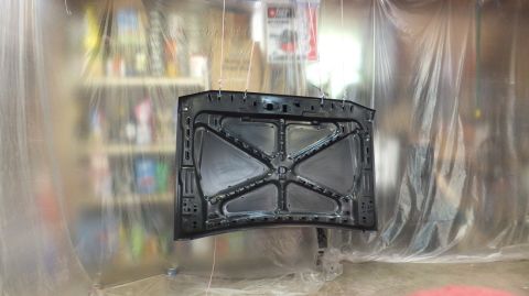 1983 Ford Bronco - The underside of a car hood is shown hanging in a spray booth, ready for refinishing.