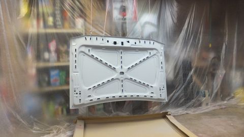 1983 Ford Bronco - A car hood's underside is painted white while suspended in a spray booth.