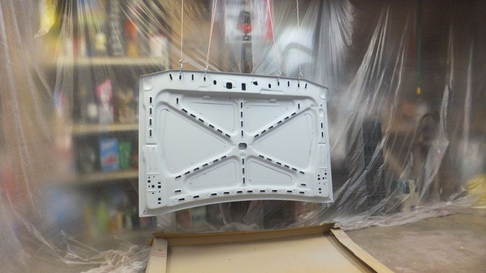 White car hood interior, suspended for painting, showing bracing and mounting points