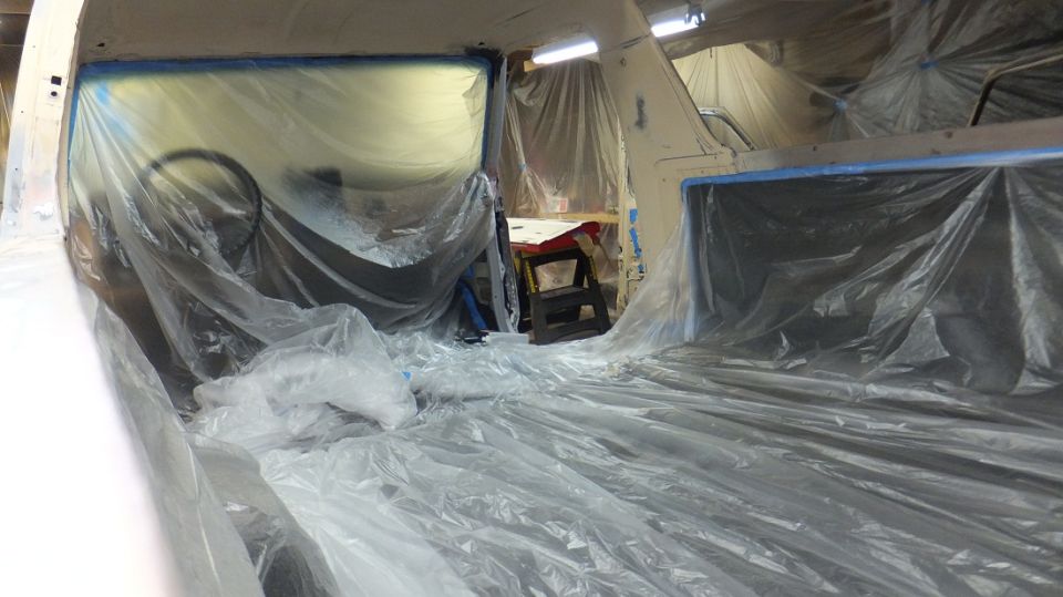 Vehicle interior covered in plastic sheeting, likely for painting. Steering wheel visible