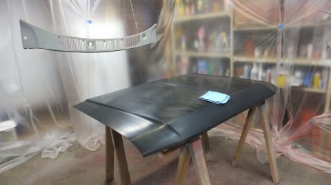 1983 Ford Bronco - A car hood and grille are prepared for painting in a workshop.