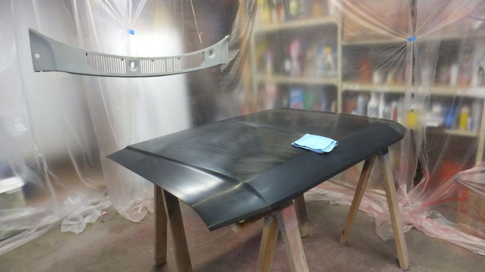 Car hood on sawhorses with a blue cloth, and a gray grille hanging above