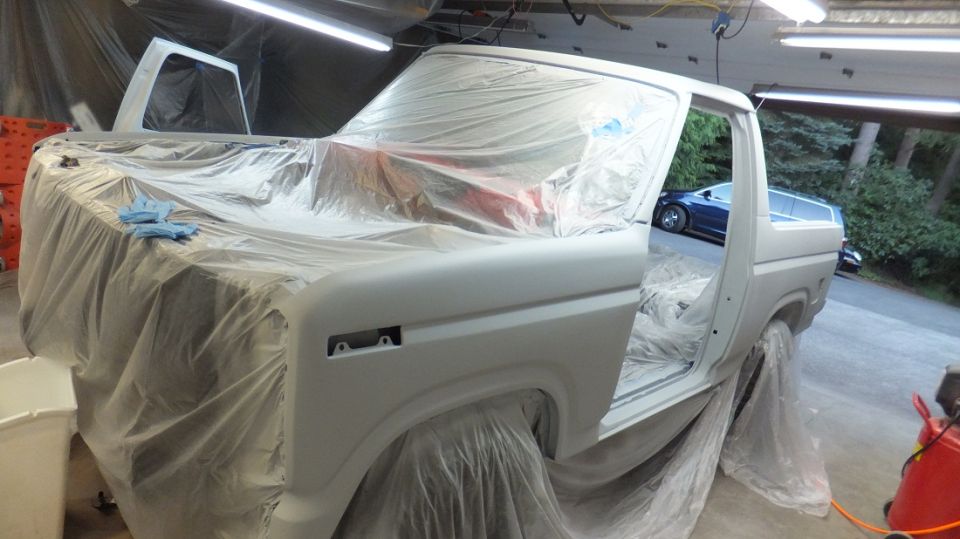 White 1980s Ford Bronco in primer, doors open, covered in plastic sheeting