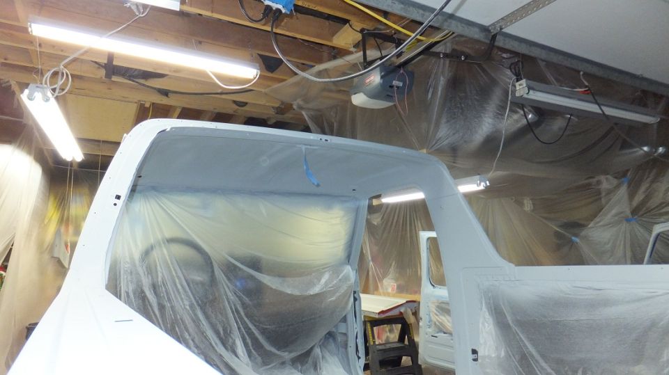 1983 Ford Bronco body covered in plastic, interior visible, in a garage with paint prep lighting