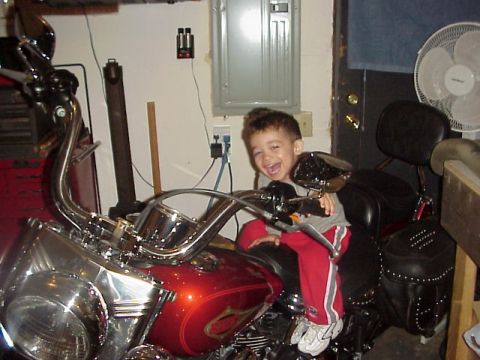 1989 Ford Bronco - A young boy smiles while sitting on a motorcycle in a garage setting.