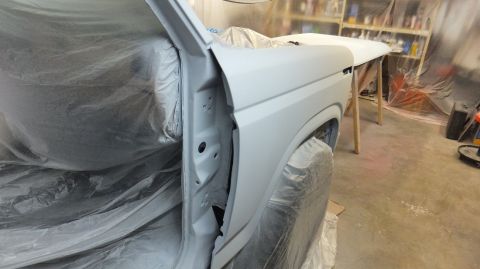 1983 Ford Bronco - A white Ford Bronco body, prepped for paint, is seen from the front quarter angle in a workshop.