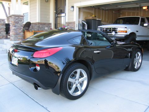 1995 Ford Bronco - A black Pontiac Solstice GXP Coupe is parked in front of a garage containing a white Ford truck.